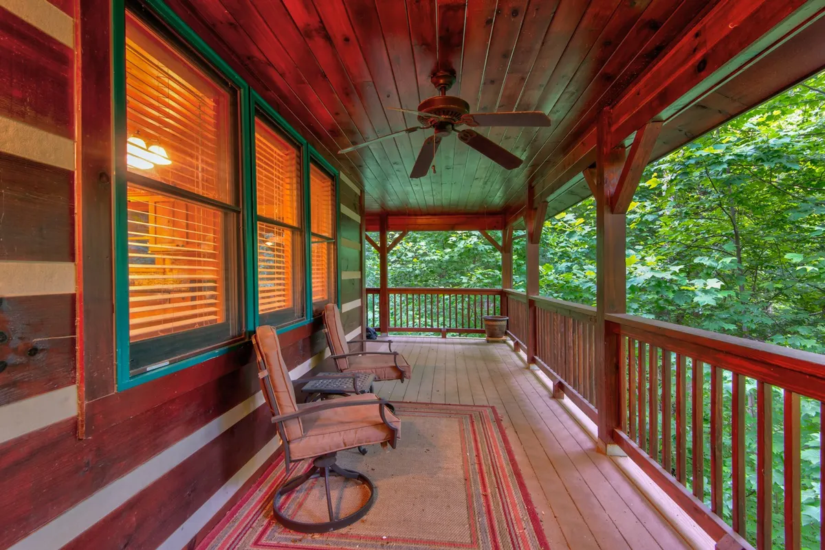 A spacious, comfortable deck area with a wooden ceiling, striped walls, cozy chairs, and a soft rug. The deck overlooks surrounding greenery, inviting guests to relax, socialize, or enjoy scenic views at any time of the day.