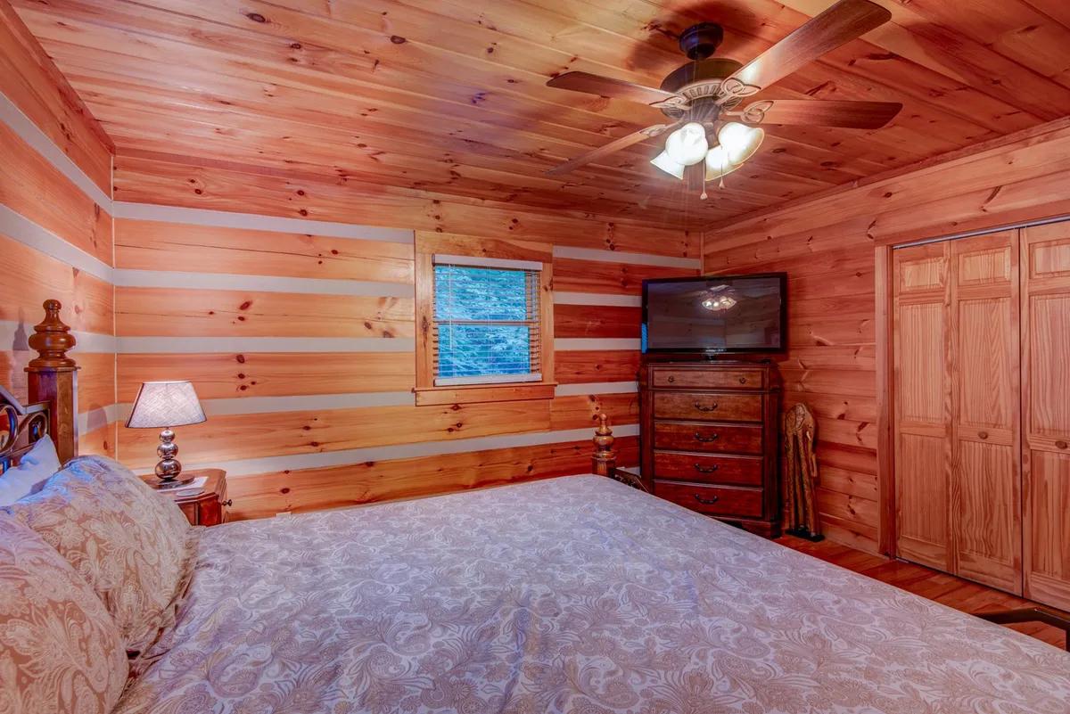 A tranquil bedroom with a wooden bed frame, decorative lamp, chest of drawers, and a window letting in natural light. The room feels peaceful and is designed for comfort and quiet rest.