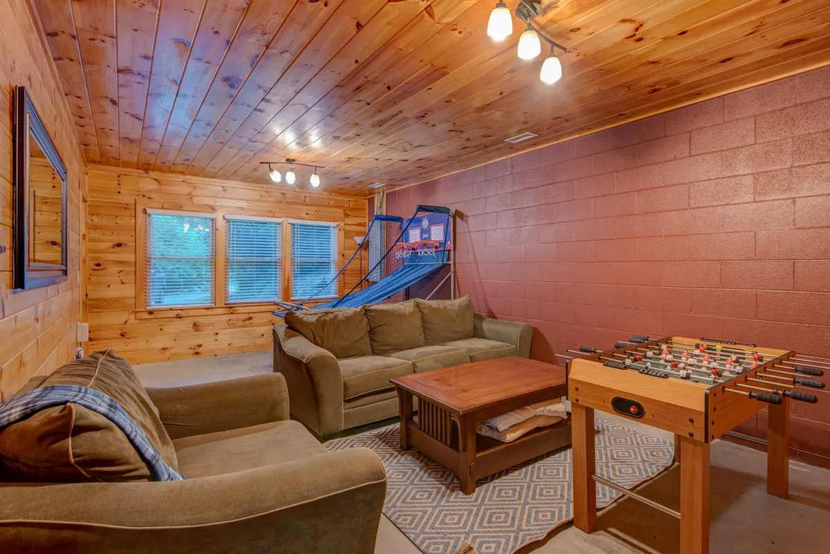 This interior shot includes a foosball table, a sofa for relaxation, and an electronic basketball hoop, all set beneath a wooden ceiling. The environment is lively yet comfortable, ideal for both active play and family movie marathons.