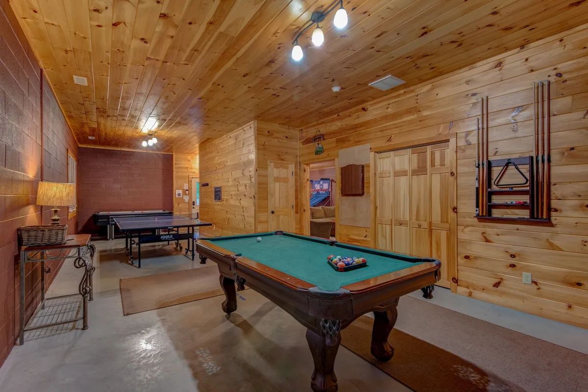 A vibrant interior game area featuring a pool table, ping pong table, and warm wood-paneled walls creates an atmosphere of play and togetherness. The room is set up for family fun, with ample space and inviting lighting for hours of entertainment, connecting to the amenities mentioned in the section.