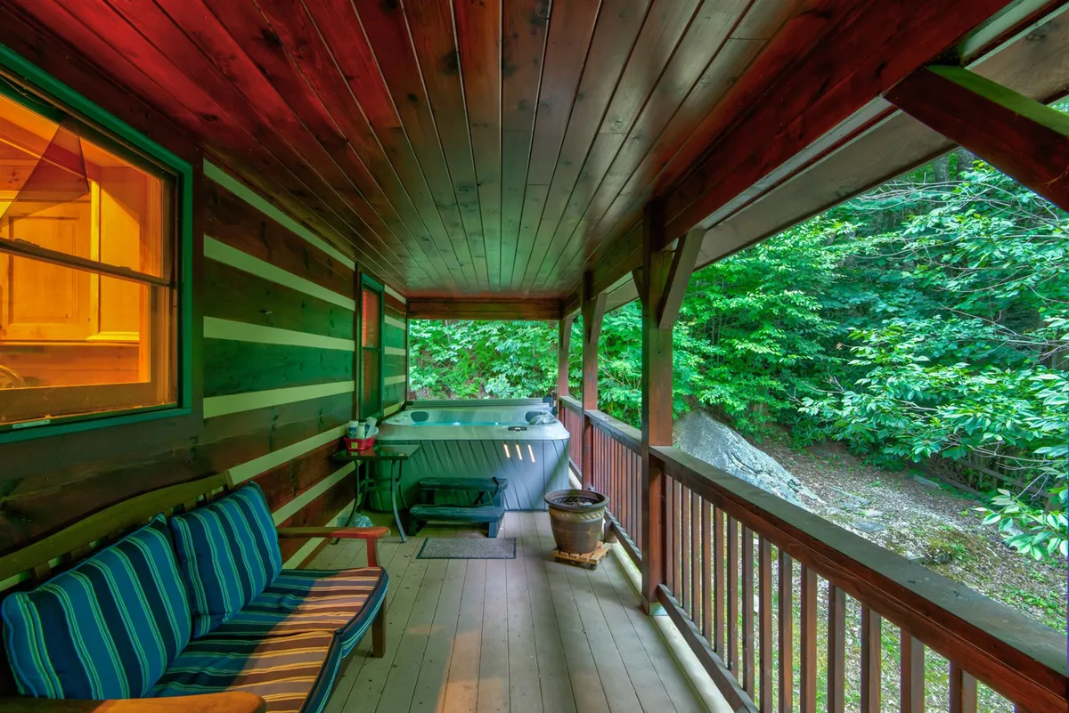 This image features a hot tub situated next to a wooden bench, framed by lush green foliage visible through the windows. The design invites guests to enjoy the connection with nature while relaxing in the warmth of the hot tub or reading on the bench.
